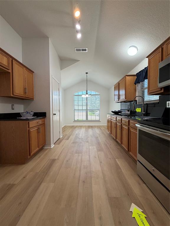 Open-concept kitchen and dining area featuring wood-finish flooring, vaulted ceilings, and an arched window Open-concept kitchen and dining area featuring wood-finish flooring, vaulted ceilings, and an arched window