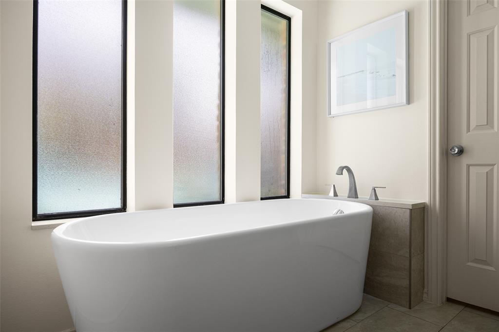 Freestanding soaking tub with brushed nickel fixtures, complemented by a stone-finish tub surround