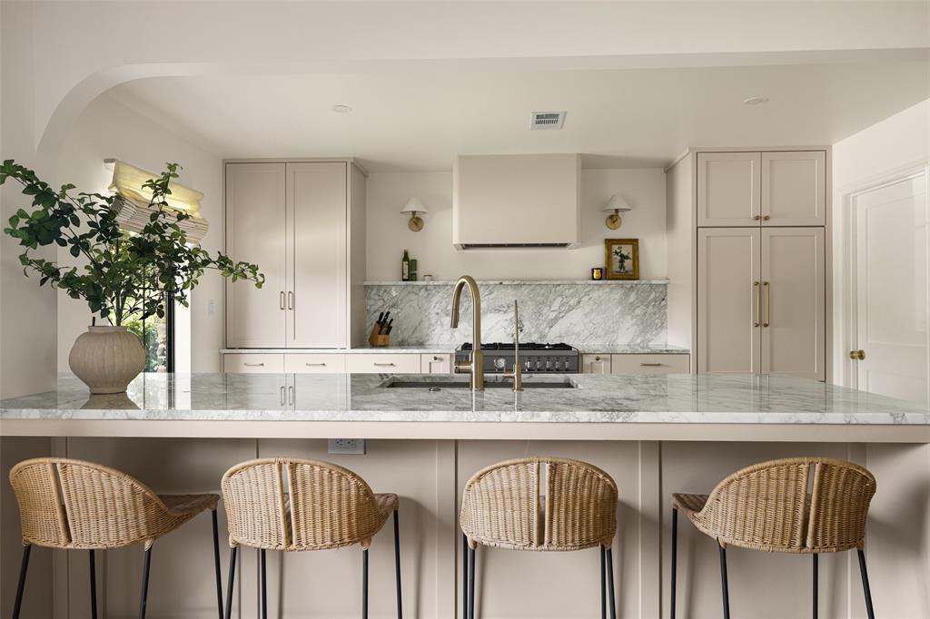 Kitchen featuring a large central island with seating, a built-in range, a substantial range hood, and a full-height marble backsplash
