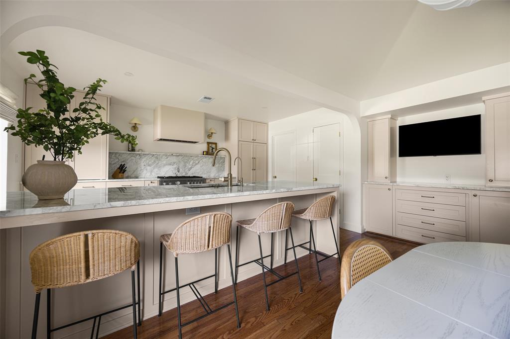 Kitchen featuring a large central island with seating, a built-in range, a marble backsplash, and ample cabinetry