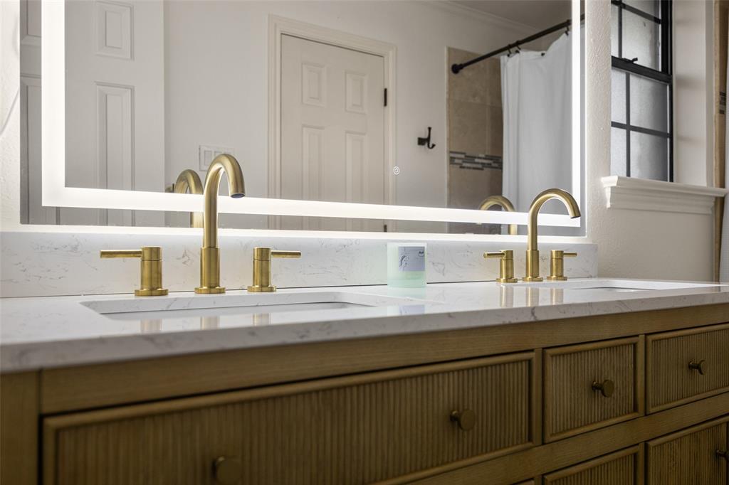 Dual vanity featuring a white countertop with integrated sinks, brushed gold faucets, and a large backlit mirror