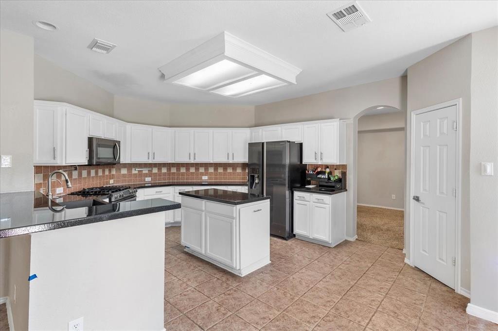 Kitchen featuring white cabinetry, a central island, dark countertops, and a tile backsplash