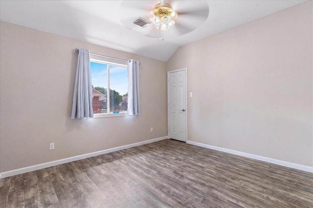 Spacious room featuring wood-finish flooring, a vaulted ceiling, and a ceiling fan with integrated lighting