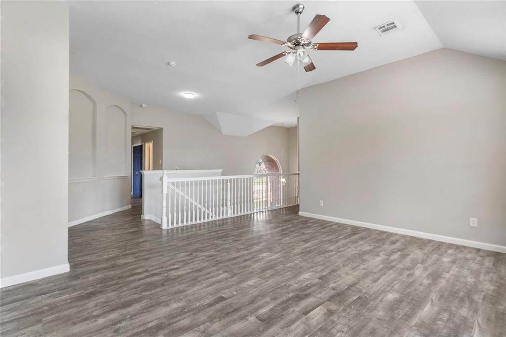 Spacious room featuring vaulted ceilings, wood-finish flooring, a contemporary ceiling fan, and a white balustrade overlooking a lower level