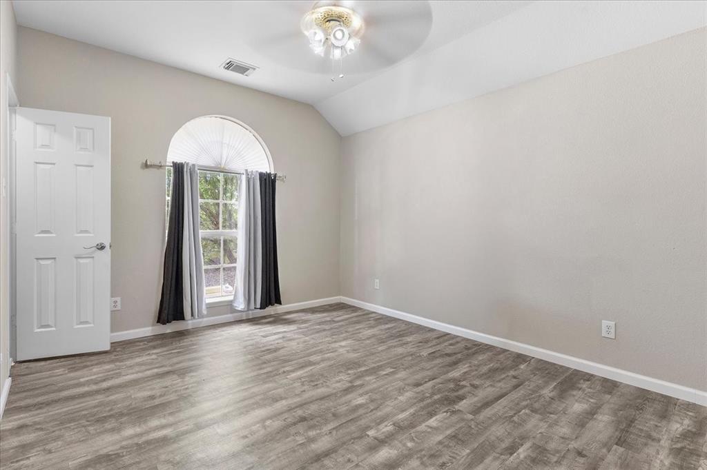 Spacious room featuring vaulted ceilings, wood-finish flooring, a large arched window, and a ceiling fan with integrated lighting