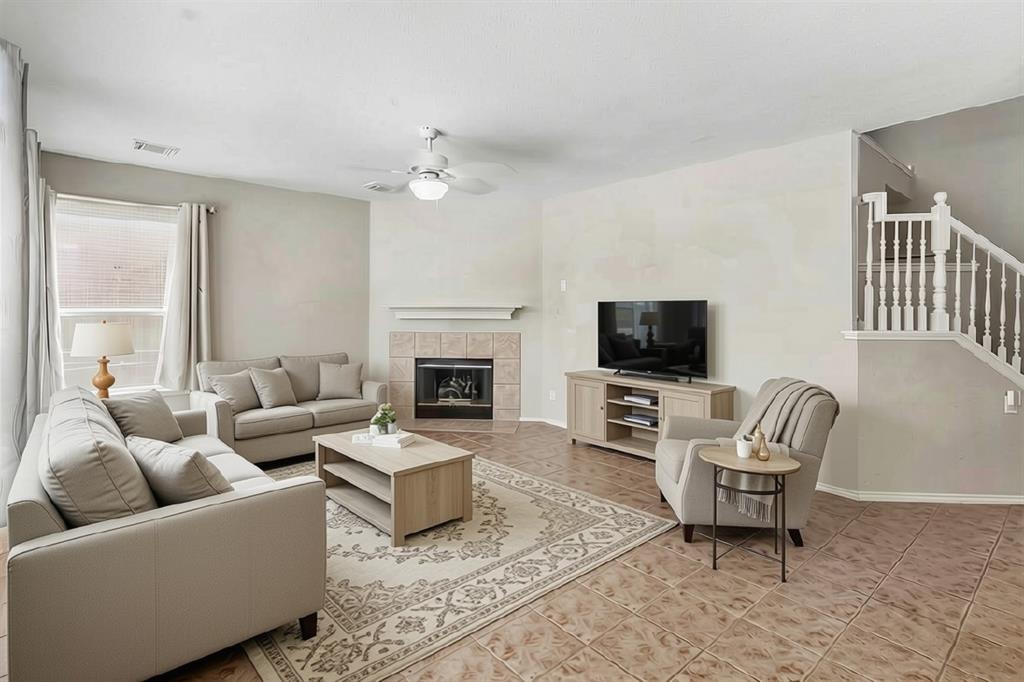 Living area featuring a tile-surround fireplace with a mantel, a ceiling fan with integrated lighting, and a white baluster staircase