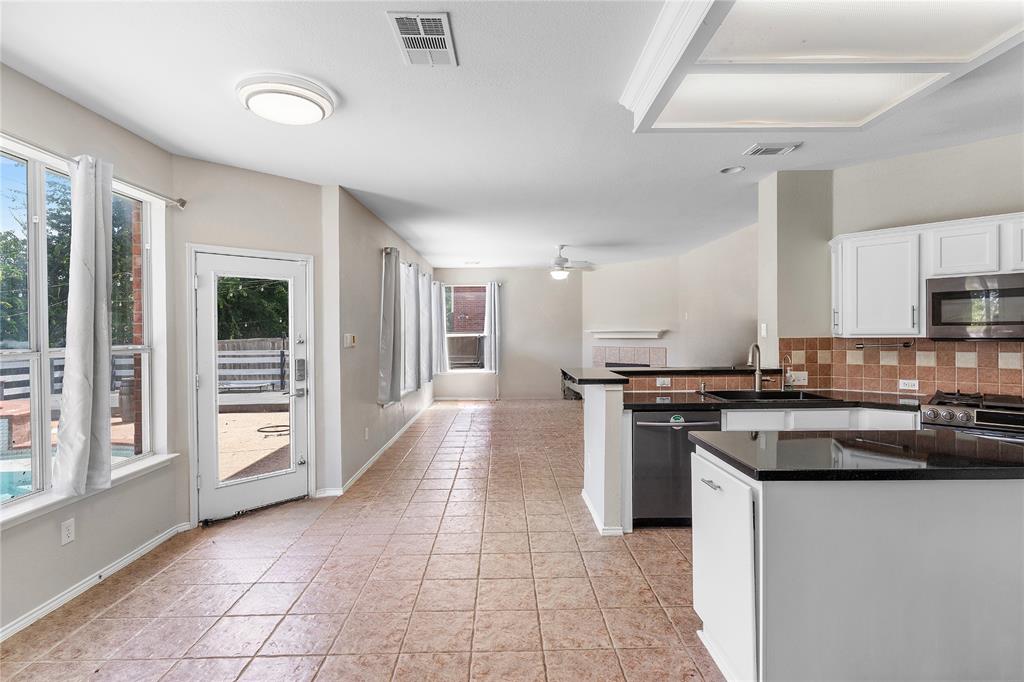 Spacious kitchen and dining area featuring white cabinetry, black granite countertops, stainless steel appliances, tile flooring, and abundant natural light from multiple windows and glass doors opening to an outdoor patio