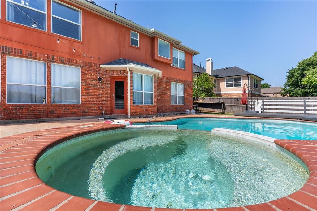 Outdoor living space featuring a brick-lined spa and swimming pool, surrounded by a concrete patio