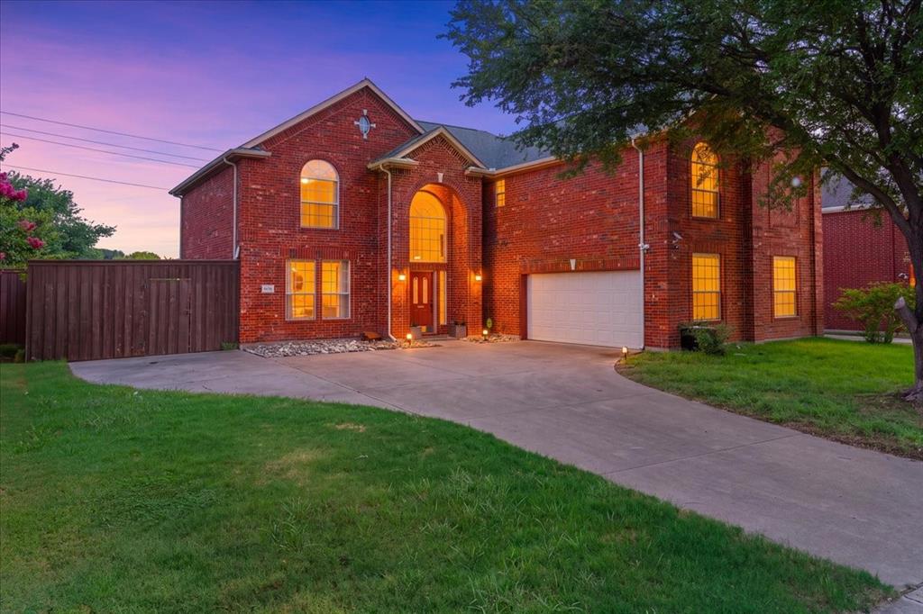 Brick exterior featuring an arched entryway with double doors, arched windows, an attached garage, and a concrete driveway