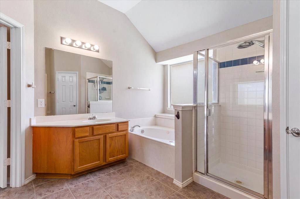 Bathroom featuring a wood-finish vanity with a single sink, a separate glass-enclosed shower, a built-in soaking tub, tile flooring, and a vaulted ceiling