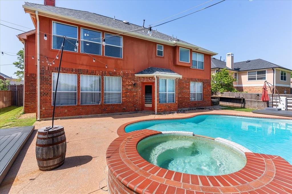 Spacious backyard featuring a freeform swimming pool and integrated hot tub with brick coping