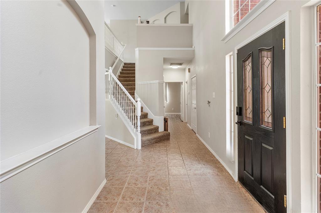 Entryway featuring a dark wood-finish door with decorative glass inserts, tile flooring, and a two-story ceiling