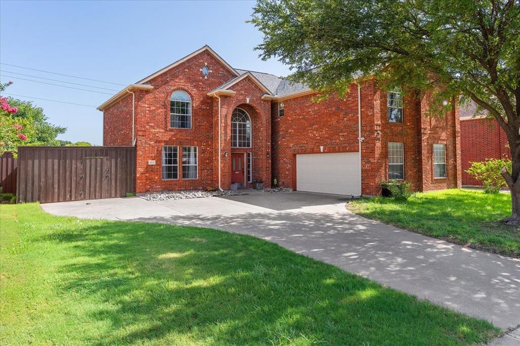 Red brick two-story residence featuring an arched entry, multiple window styles including arched and rectangular, an attached garage, and a concrete driveway