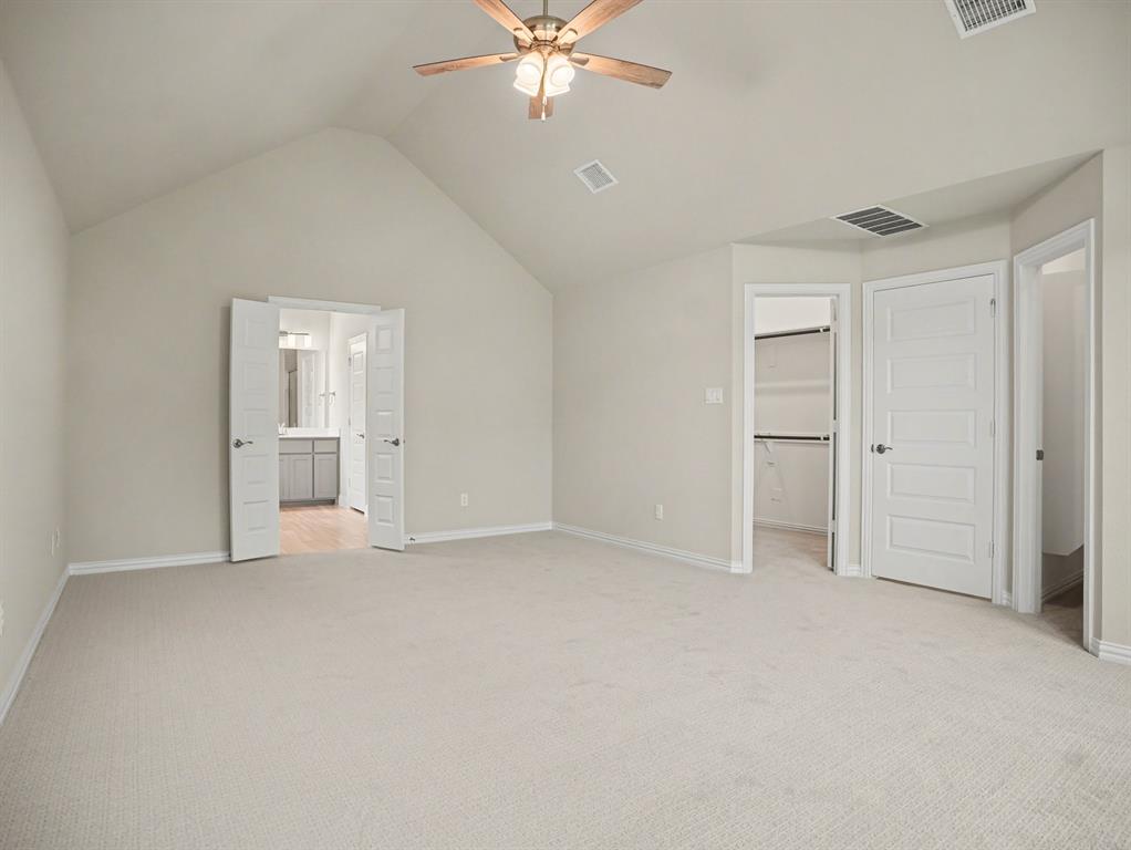 Spacious room featuring vaulted ceilings, light-toned carpeting, a ceiling fan with integrated lighting, and multiple access points including a double door entry to a bathroom and a closet with built-in shelving
