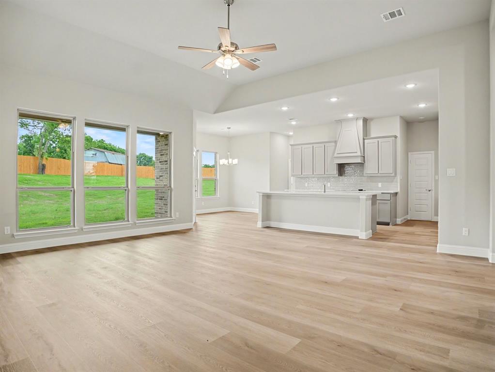 Open-concept living area featuring light wood-finish flooring, a vaulted ceiling with a ceiling fan, and multiple large windows