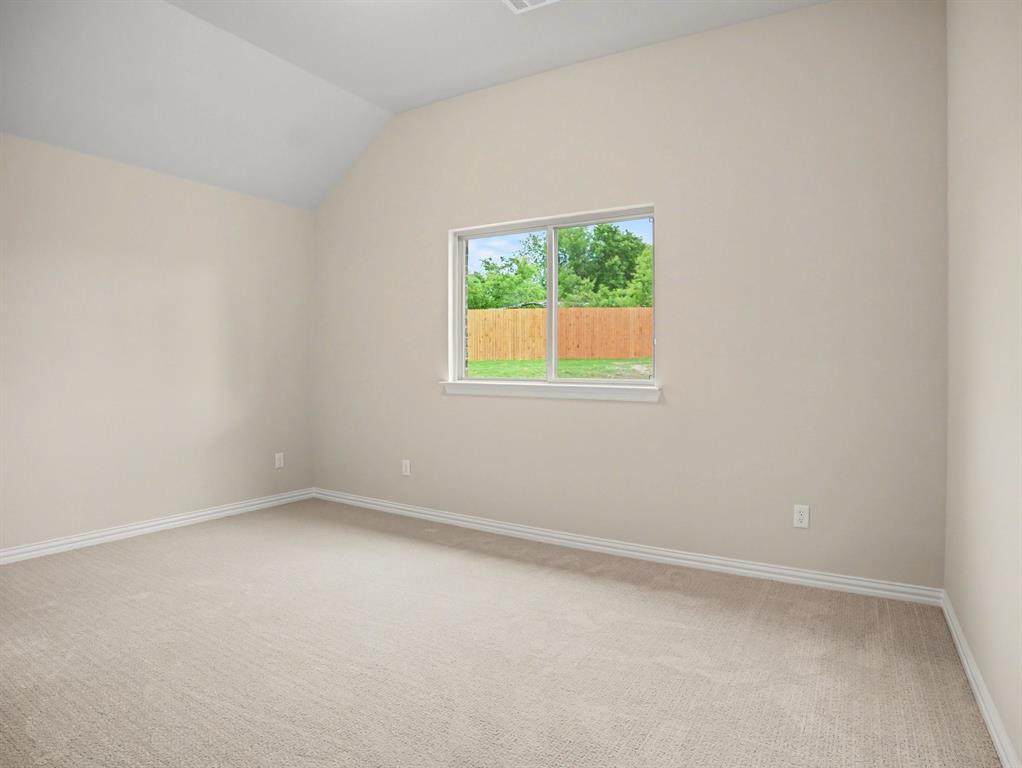 Vaulted ceiling bedroom featuring plush neutral carpeting, white baseboards, and a large window with a wood fence backdrop