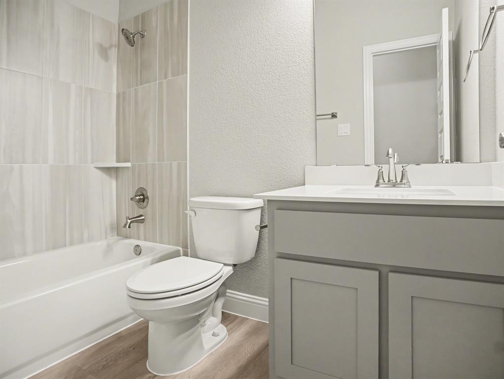 Bathroom featuring a white bathtub, a toilet, and a vanity with a white countertop and gray cabinetry