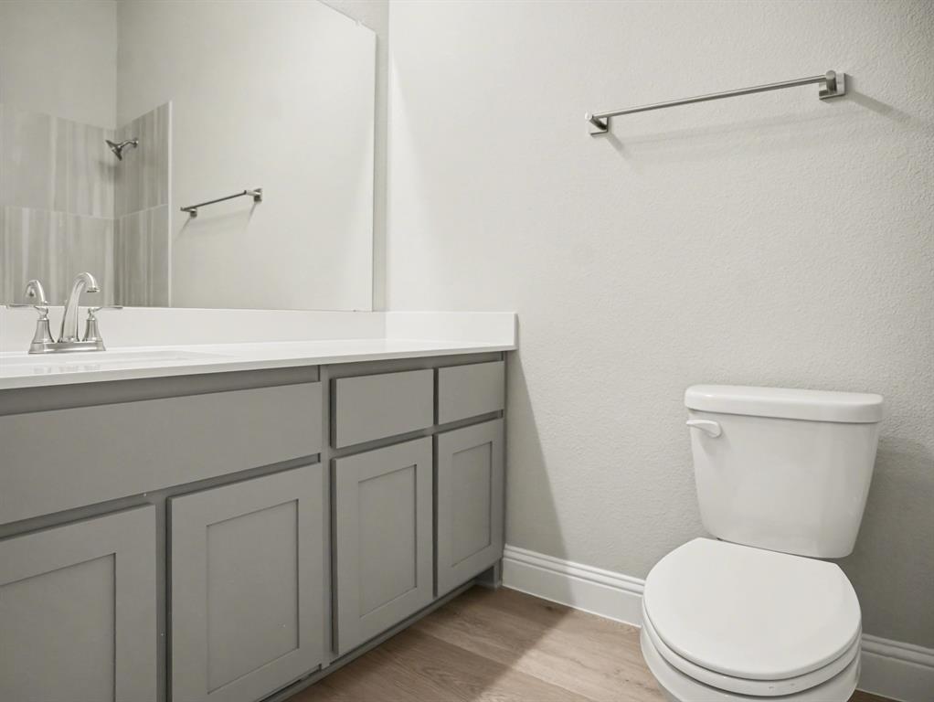 Bathroom featuring a white countertop with an integrated sink, brushed nickel faucet, large vanity mirror, light grey shaker-style cabinetry, and wood-finish flooring