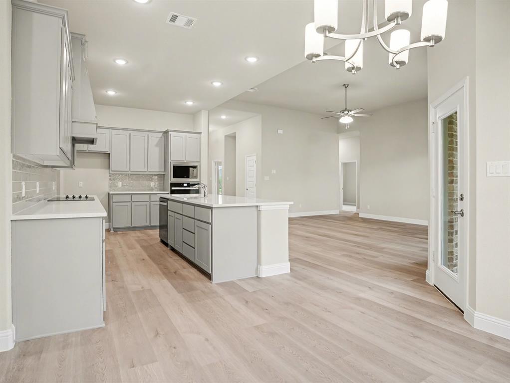 Modern kitchen featuring light gray cabinetry, a white countertop island, integrated microwave and oven, a white cooktop, and light wood-finish flooring