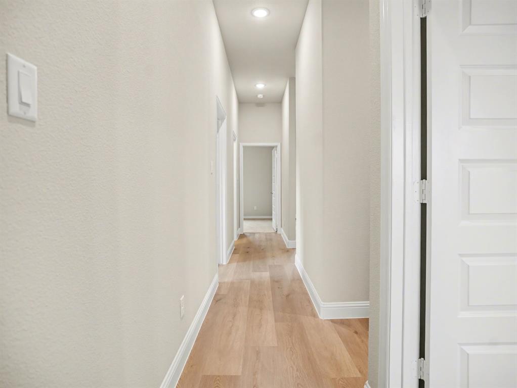 Elongated hallway featuring wood-finish flooring, recessed lighting, neutral wall tones, and white trim