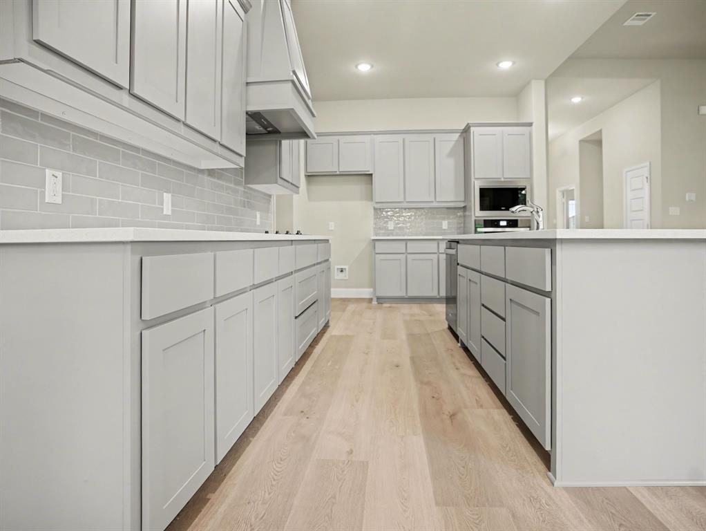 Contemporary kitchen featuring light gray shaker cabinetry, white countertops, a subway tile backsplash, and light wood-finish flooring