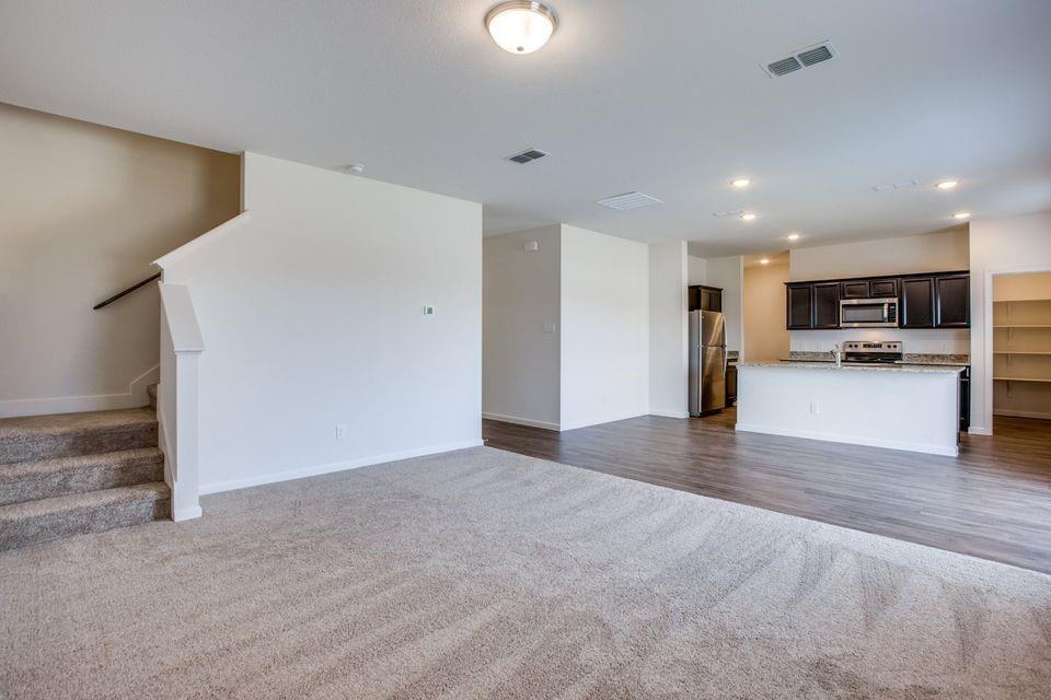 Open-concept living area featuring a kitchen with dark wood-finish cabinetry, stainless steel appliances, and a breakfast bar with a light-toned countertop Open-concept living area featuring a kitchen with dark wood-finish cabinetry, stainless steel appliances, and a breakfast bar with a light-toned countertop