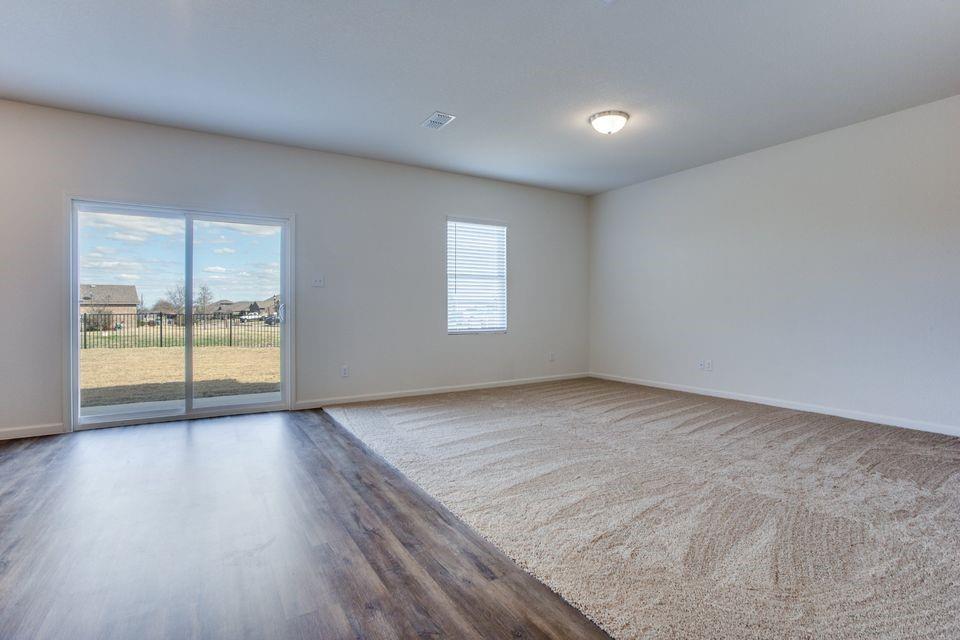 Spacious room featuring a sliding glass door, a single window with blinds, wood-finish flooring, and light-toned carpeting Spacious room featuring a sliding glass door, a single window with blinds, wood-finish flooring, and light-toned carpeting