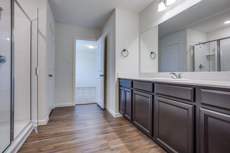 Spacious bathroom featuring wood-finish flooring, a glass-enclosed shower, and a vanity with a light-colored countertop Spacious bathroom featuring wood-finish flooring, a glass-enclosed shower, and a vanity with a light-colored countertop