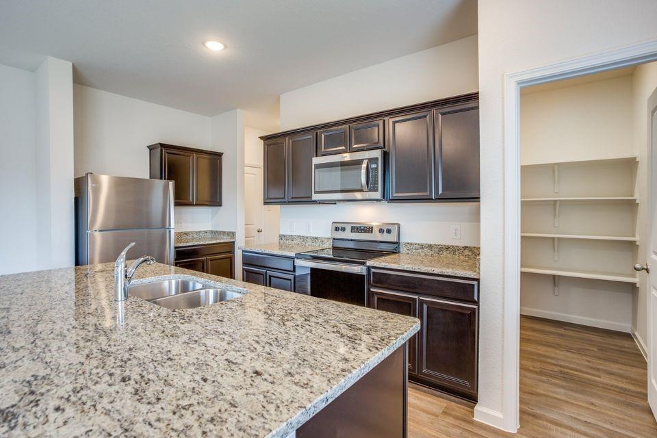 Kitchen featuring an island with a stainless steel double basin sink, dark wood-finish cabinetry, stainless steel appliances, speckled stone countertops, and wood-finish flooring Kitchen featuring an island with a stainless steel double basin sink, dark wood-finish cabinetry, stainless steel appliances, speckled stone countertops, and wood-finish flooring