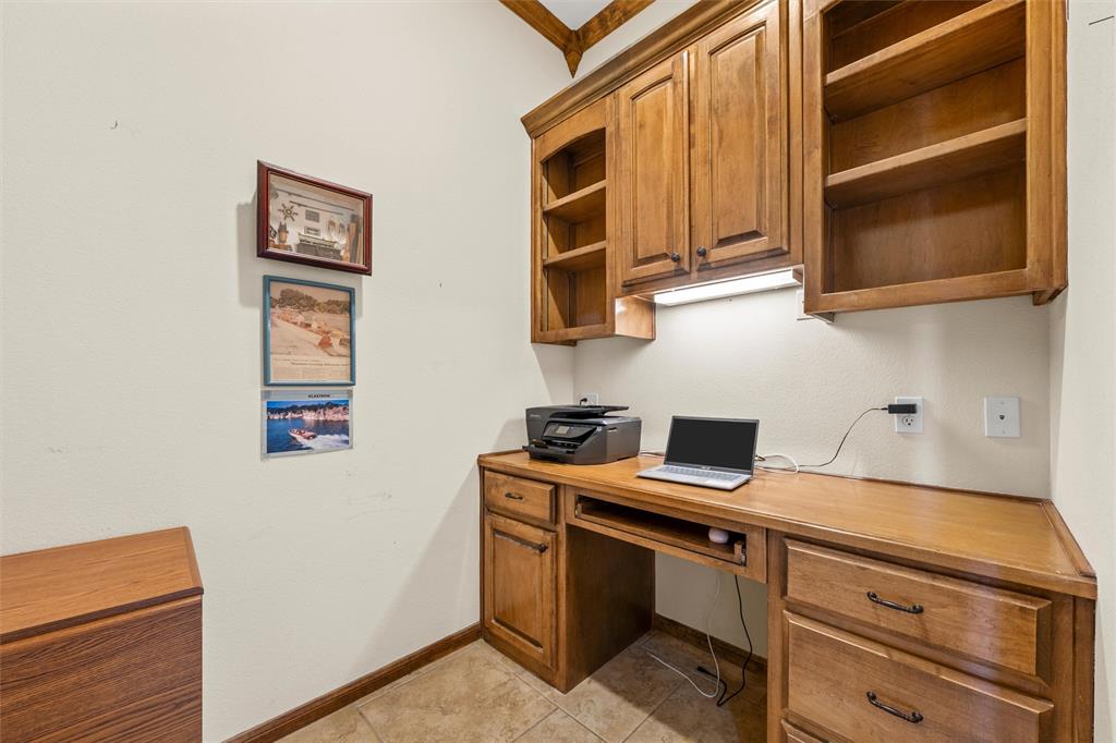 Built-in desk area featuring wood-finish cabinetry, integrated shelving, under-cabinet lighting, and tile flooring Built-in desk area featuring wood-finish cabinetry, integrated shelving, under-cabinet lighting, and tile flooring