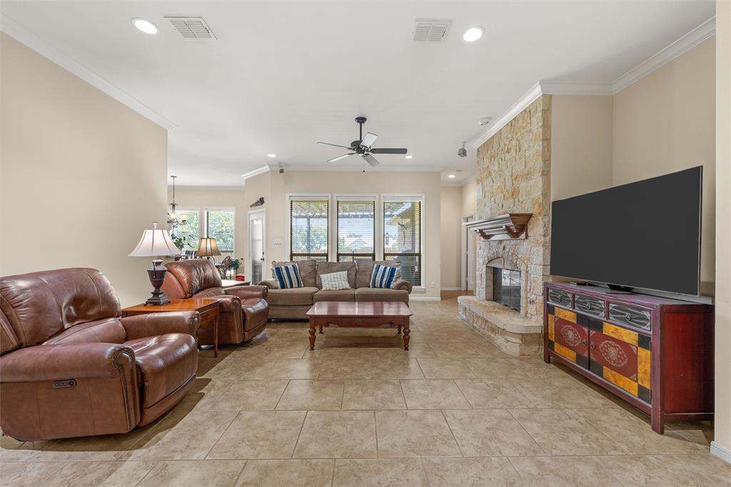 Expansive living area featuring tile flooring, a stone-clad fireplace with a wood mantel, crown molding, and recessed lighting