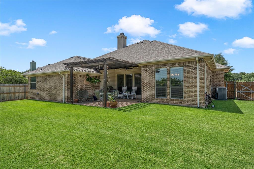 Expansive green lawn bordering a brick exterior with a rear patio featuring a wooden pergola Expansive green lawn bordering a brick exterior with a rear patio featuring a wooden pergola