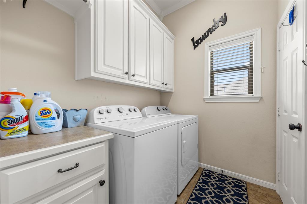 Dedicated laundry space featuring upper and lower cabinetry with black hardware, a window with horizontal blinds, and a tiled floor