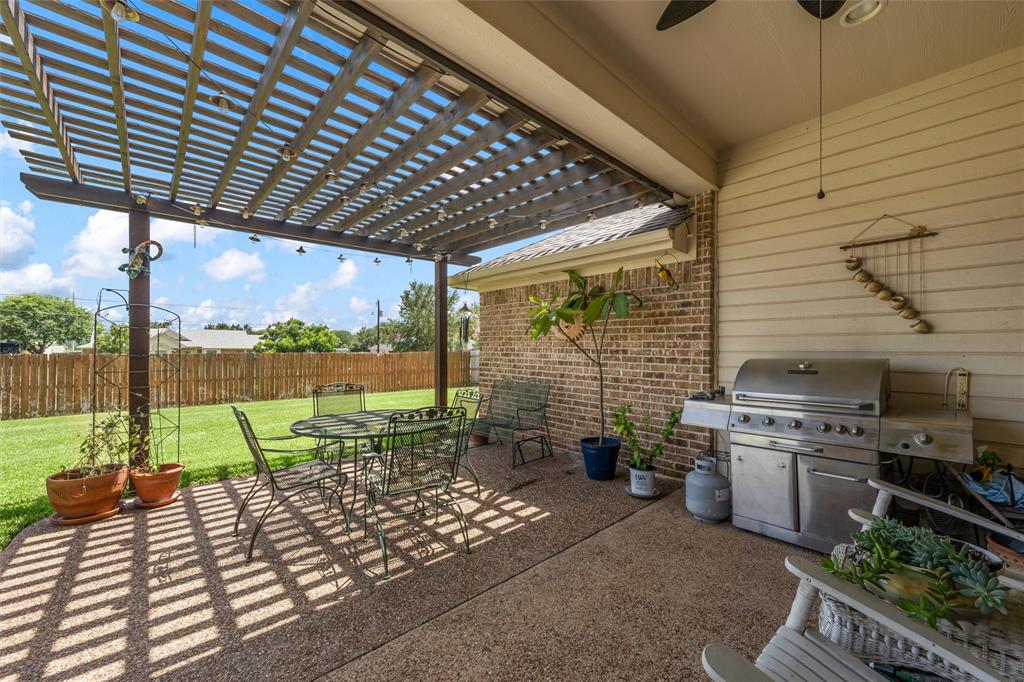 Covered patio area featuring a wooden pergola, an exposed aggregate concrete slab, a ceiling fan, and a brick exterior wall Covered patio area featuring a wooden pergola, an exposed aggregate concrete slab, a ceiling fan, and a brick exterior wall