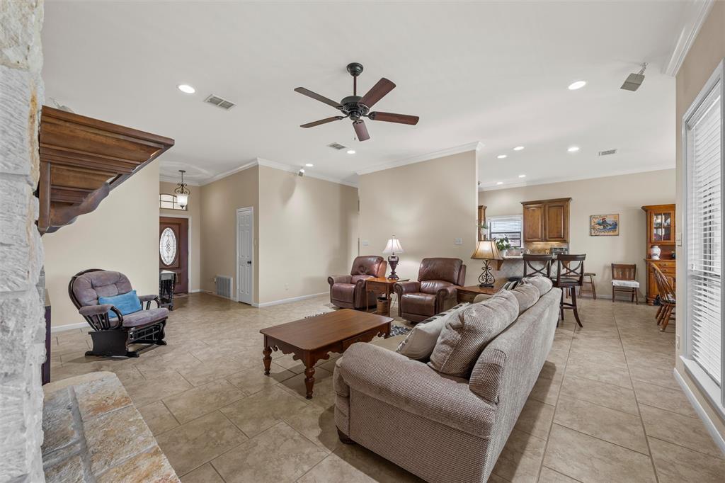 Spacious living area featuring tiled flooring, a stone fireplace surround, and crown molding