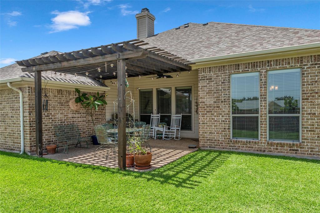 Expansive backyard featuring a pergola-covered patio with string lighting, brick exterior, and a manicured lawn