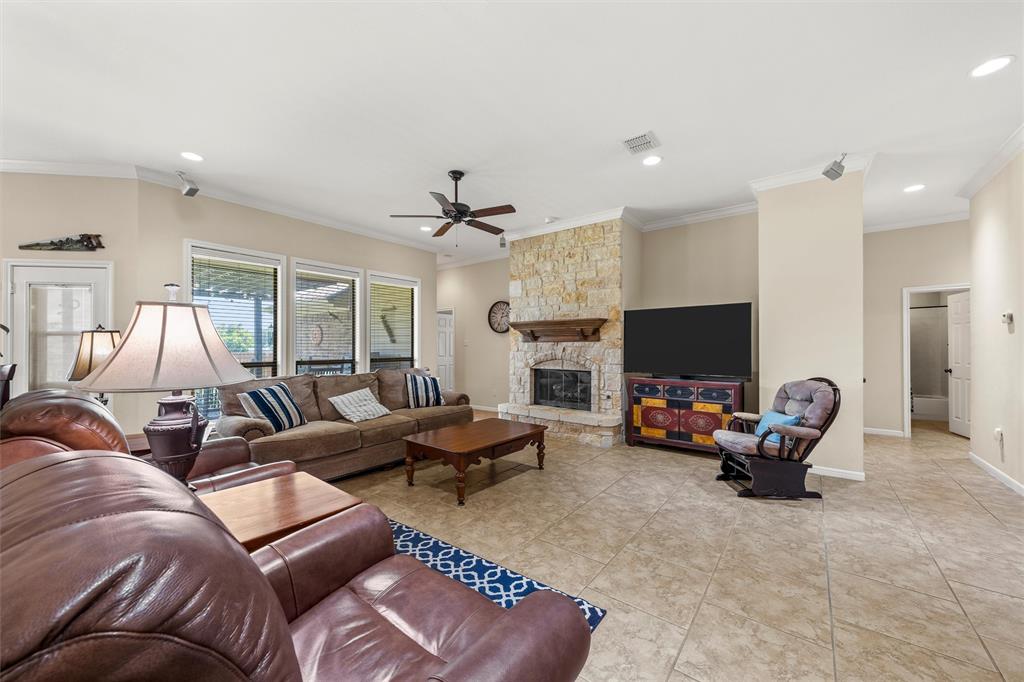 Spacious living area featuring a stone fireplace with a wood mantel, large format tile flooring, crown molding, and recessed lighting
