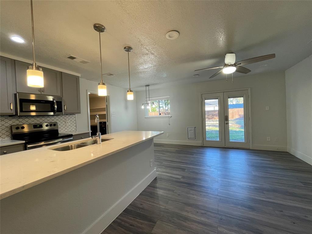 Kitchen with gray cabinetry, backsplash, dark hardwood / wood-style flooring, light stone countertops, and stainless steel appliances