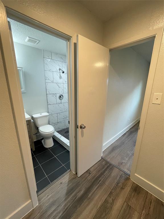 Bathroom featuring vanity, a textured ceiling, a tile shower, hardwood / wood-style flooring, and toilet