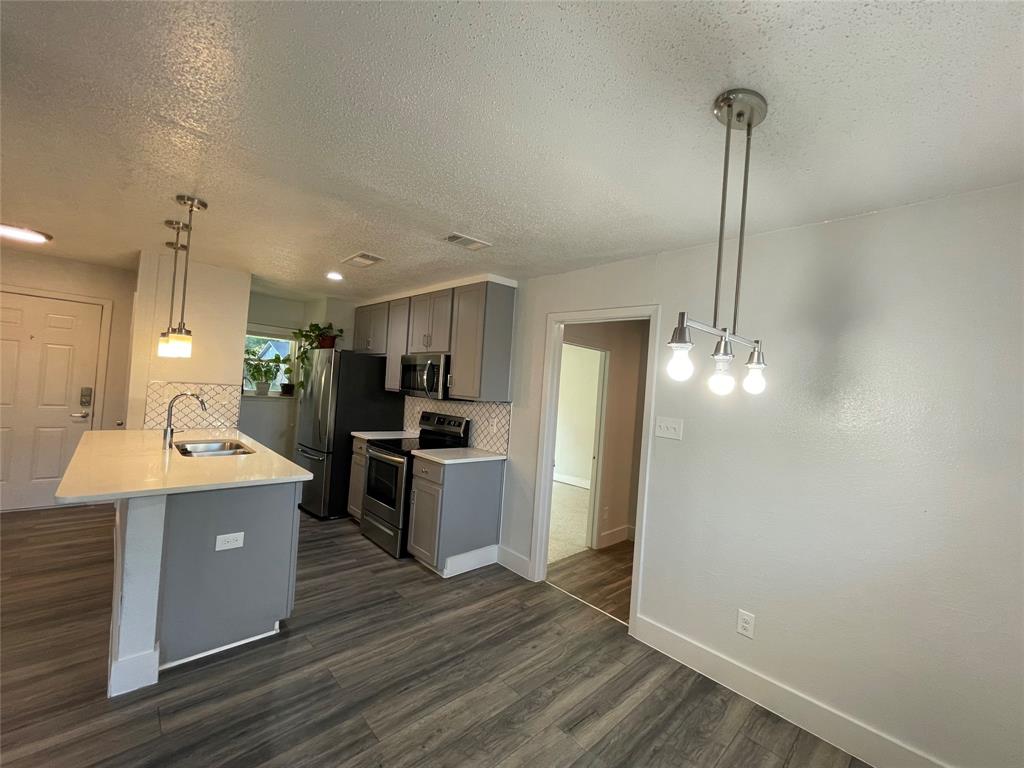 Kitchen featuring sink, decorative backsplash, appliances with stainless steel finishes, decorative light fixtures, and dark hardwood / wood-style flooring