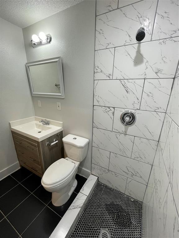Bathroom with a tile shower, a textured ceiling, tile patterned floors, vanity, and toilet