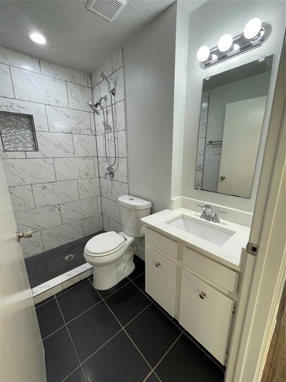 Bathroom with tile patterned floors, toilet, vanity, and tiled shower