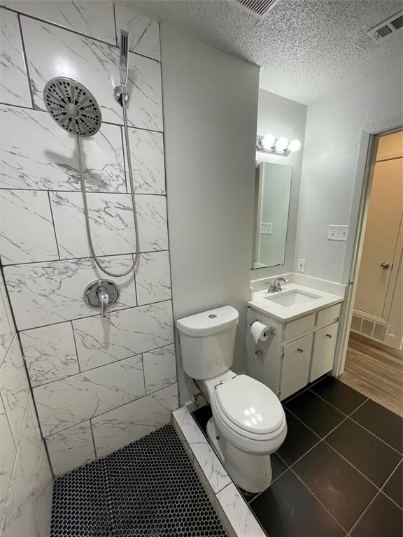 Bathroom featuring tiled shower, vanity, a textured ceiling, tile patterned flooring, and toilet