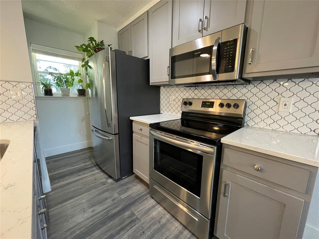 Kitchen with light stone counters, tasteful backsplash, gray cabinets, stainless steel appliances, and dark hardwood / wood-style floors