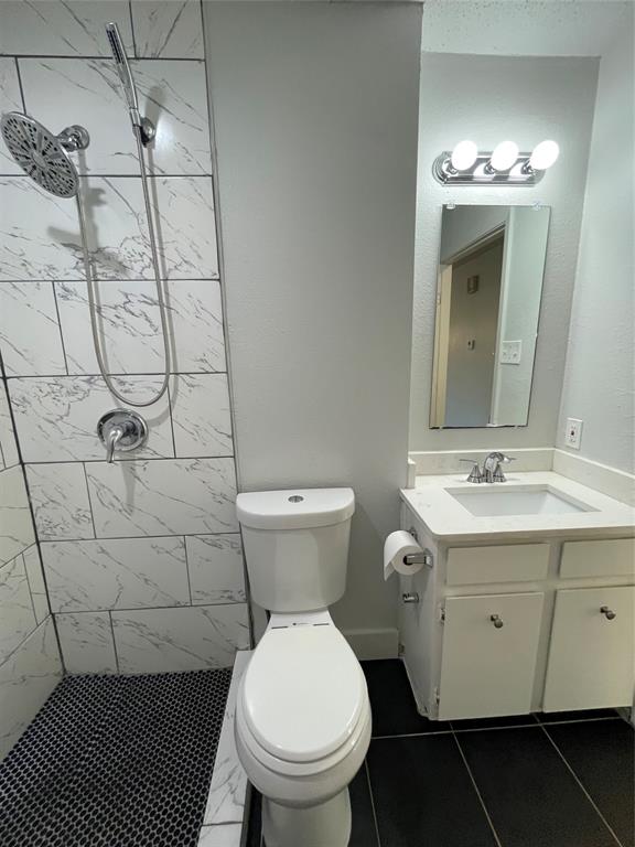 Bathroom featuring vanity, tile patterned floors, toilet, and tiled shower