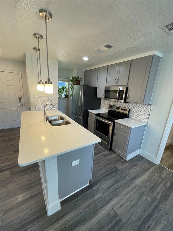 Kitchen featuring dark wood-type flooring, backsplash, stainless steel appliances, decorative light fixtures, and sink