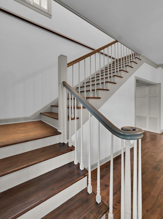 Staircase featuring wood-finish treads and risers, a white baluster system, and a dark handrail with a decorative scroll newel post