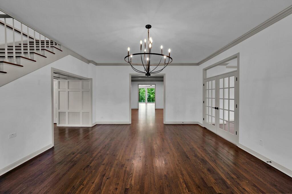 Spacious room featuring rich wood-finish flooring, a contemporary black metal chandelier, white walls with gray crown molding, and a staircase with white risers and dark wood treads