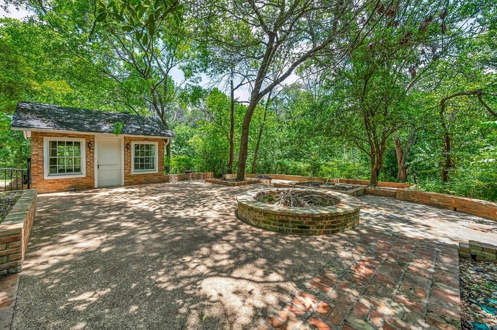 Expansive outdoor patio area featuring a built-in brick fire pit, a dedicated brick outbuilding, and mature trees providing natural canopy