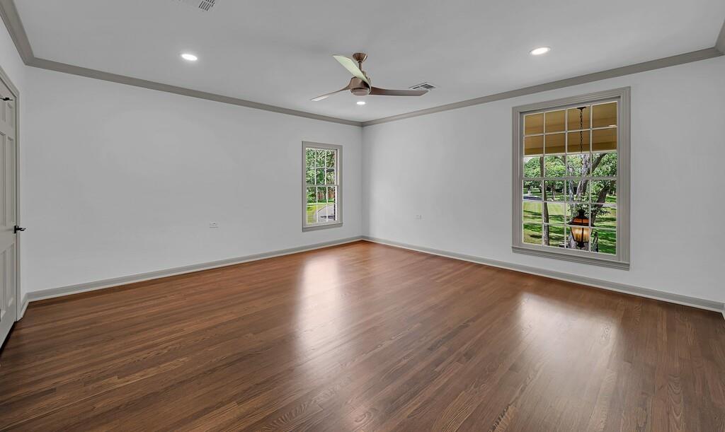 Spacious room featuring wood-finish flooring, two large windows with exterior views, crown molding, a ceiling fan, and recessed lighting